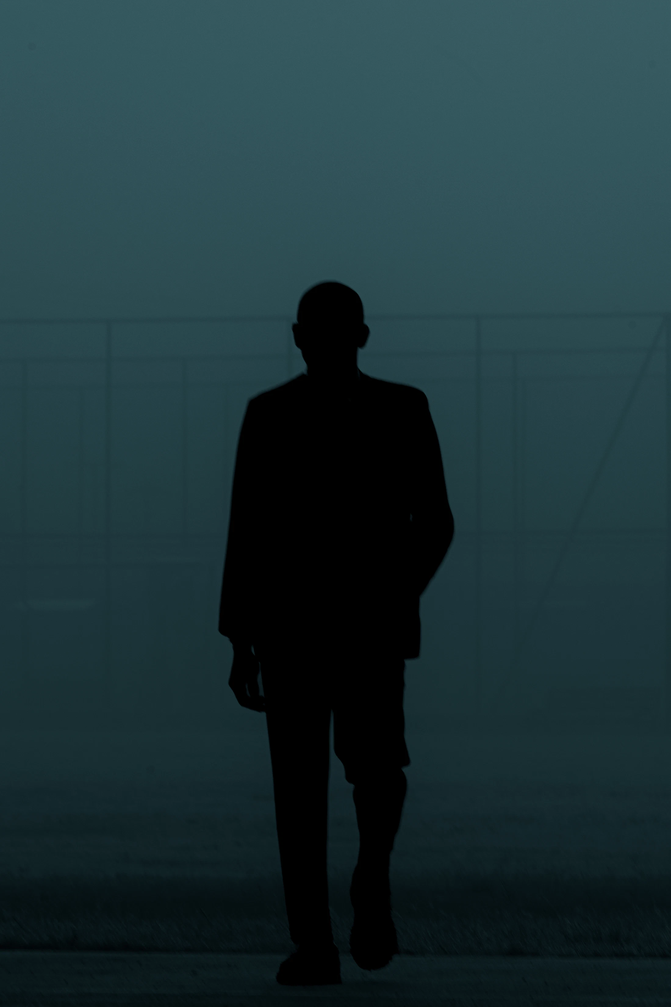 Silhouette of a person in a suit walking through a dark, backlit space