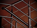 A close-up of a modern metal railing structure, featuring intersecting horizontal and vertical bars. The metallic elements contrast against a warm, brownish background, highlighting the sleek and polished nature of the metal.
