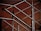 A close-up of a modern metal railing structure, featuring intersecting horizontal and vertical bars. The metallic elements contrast against a warm, brownish background, highlighting the sleek and polished nature of the metal.