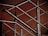 A close-up of a modern metal railing structure, featuring intersecting horizontal and vertical bars. The metallic elements contrast against a warm, brownish background, highlighting the sleek and polished nature of the metal.
