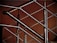 A close-up of a modern metal railing structure, featuring intersecting horizontal and vertical bars. The metallic elements contrast against a warm, brownish background, highlighting the sleek and polished nature of the metal.