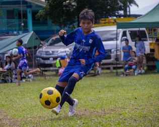 a young boy kicking a soccer ball on a field