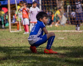 a young boy sitting on the ground during a soccer game