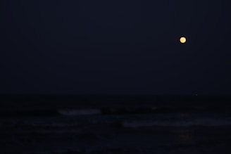 A serene night sky filled with stars and a glowing moon over calm ocean waves.