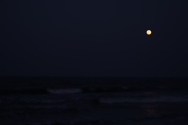 A serene night sky filled with stars and a glowing moon over calm ocean waves.