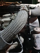 A close-up view of an engine compartment featuring braided hoses, fastened with metal clamps. The setting is dimly lit, highlighting the textures and patterns of the hoses and surrounding machinery components.