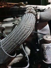 A close-up view of an engine compartment featuring braided hoses, fastened with metal clamps. The setting is dimly lit, highlighting the textures and patterns of the hoses and surrounding machinery components.