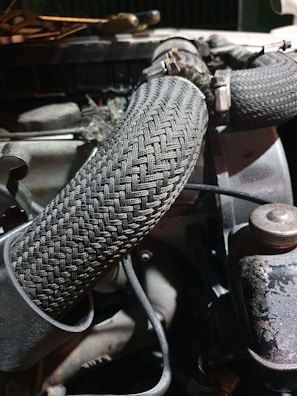A close-up view of an engine compartment featuring braided hoses, fastened with metal clamps. The setting is dimly lit, highlighting the textures and patterns of the hoses and surrounding machinery components.