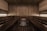 A wooden sauna room with benches lining the walls and a central heating element filled with stones. The warm tones of the wood create a cozy atmosphere, enhanced by soft lighting.