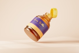 A honey bottle with a golden cap that is partially open and appears to be floating against a soft beige background. The bottle has a purple and yellow label with the words 'Honey Bottle' printed on it.