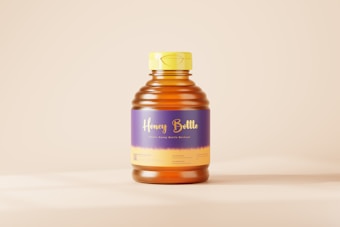 A plastic honey bottle with a yellow cap and a label featuring purple and yellow colors. The label has the words 'Honey Bottle' in a cursive font. The bottle is placed against a plain, light beige background.