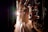 Ballet dancers in elegant tutus walk towards the stage, illuminated by bright stage lights. The scene captures the backstage area with various stage equipment visible.