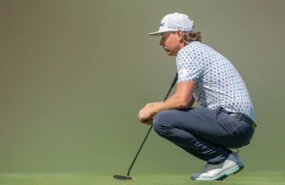 Golfer adjusting the adjustable waistband of the Pro Signature trousers beside a green fairway.