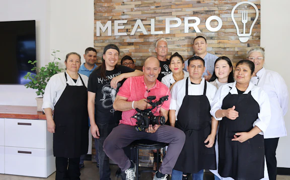 A warm group photo of the seven team members smiling in the restaurant kitchen.