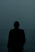 Silhouette of a man standing against a foggy, dark forest background.