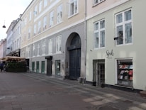 A street with buildings showcasing large windows and an arched doorway. A small bookshop named 'Soul Books' is visible with books displayed in the window. A restaurant with an outdoor seating area covered in an awning is situated further along the street. Cobblestone pavement adds a historical touch, and there are bicycles parked along the sidewalk.