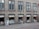 A row of windows on an urban building with a small bookstore at the ground level. The shop displays a variety of books and promotional material in the windows under the sign 'Bøger & Kuriosa'. Above the shop, there are several identical windows on a gray facade.