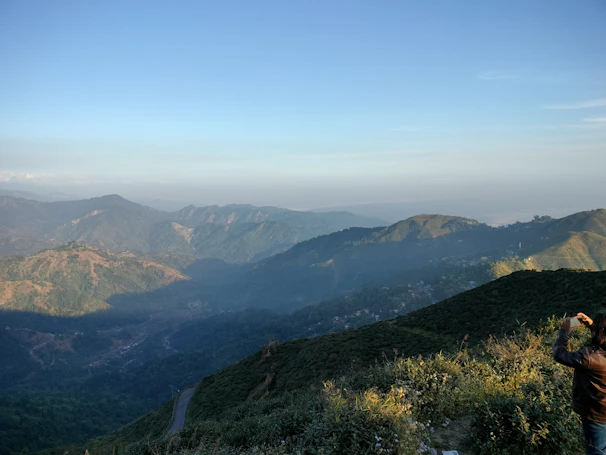 A traveler capturing a panoramic mountain view from a rocky summit.
