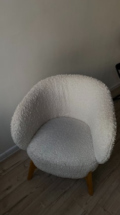 Upholstered accent armchair with wooden legs set against a calming neutral wall.