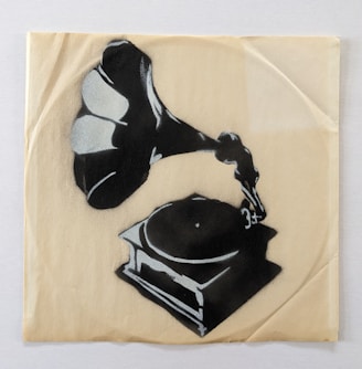 A stencil-style artwork of a gramophone on a textured, beige surface. The gramophone is shaded in black, with highlights in white to give a three-dimensional effect. The simplicity of the design contrasts with the detailed shadowing, giving it an artistic appeal.