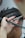 A close-up of a haircut in progress, focusing on a section of short dark hair being trimmed with scissors. A hand is steadying the hair with a comb, and a few small hair clippings are visible.