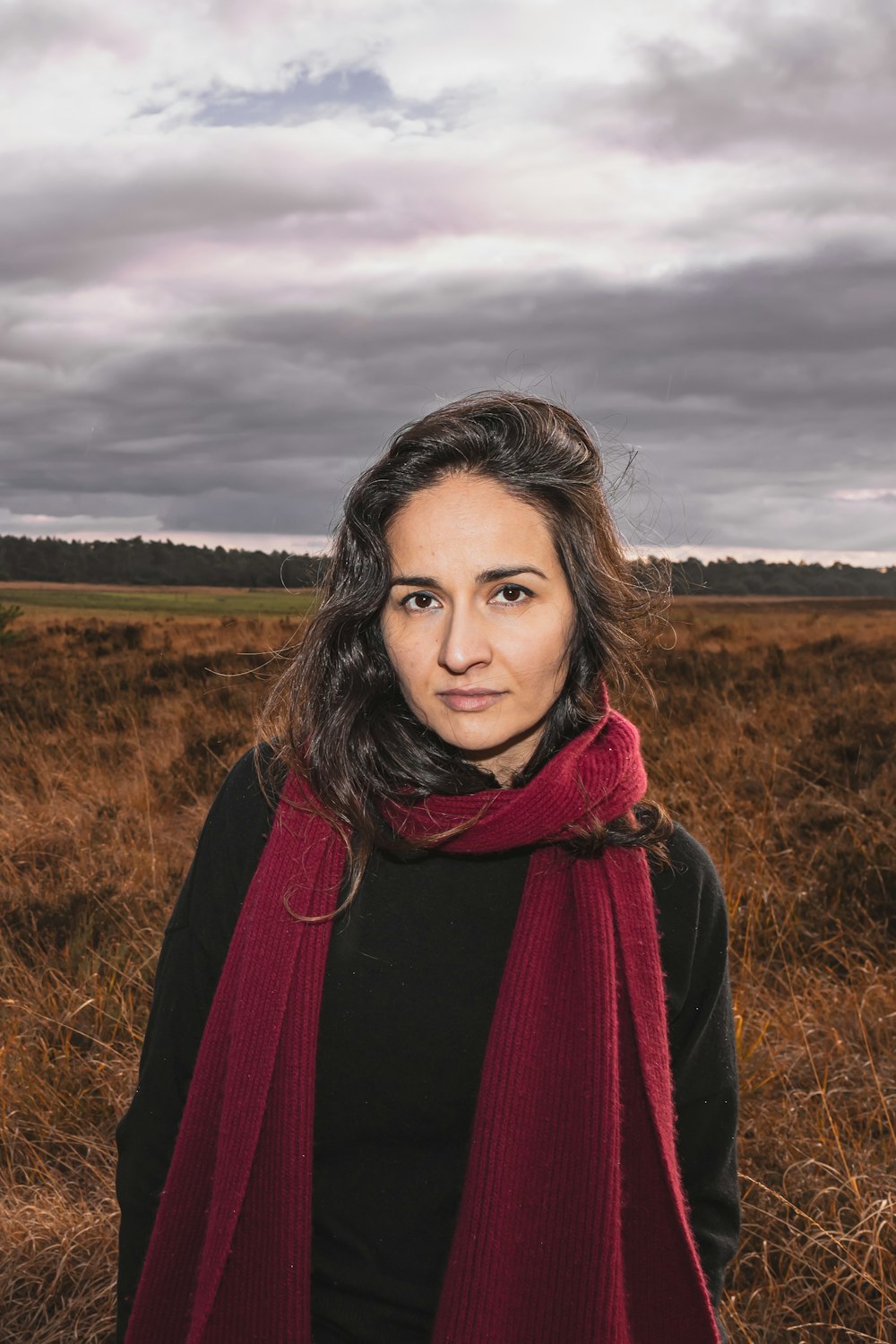 a woman standing in a field wearing a red scarf