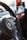 The image features a close-up view of a car's interior, specifically focusing on a Volkswagen steering wheel. Adjacent to the steering wheel, various controls and a portion of the dashboard are visible. A red and white keychain or accessory is hanging, and part of the car's air vents and infotainment system is present.