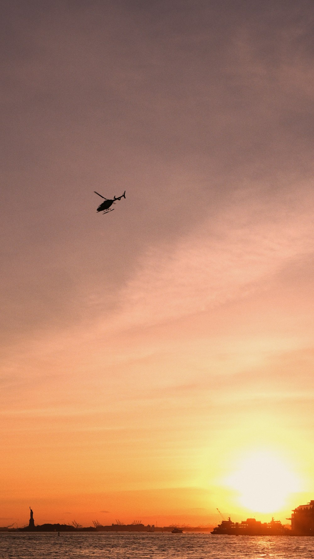 a helicopter flying over a body of water at sunset