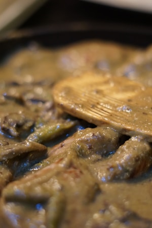 A close-up view of a creamy dish with visible chunks and a wooden spatula partially submerged in the mixture. The texture appears thick and smooth, with a glossy sheen reflecting light.
