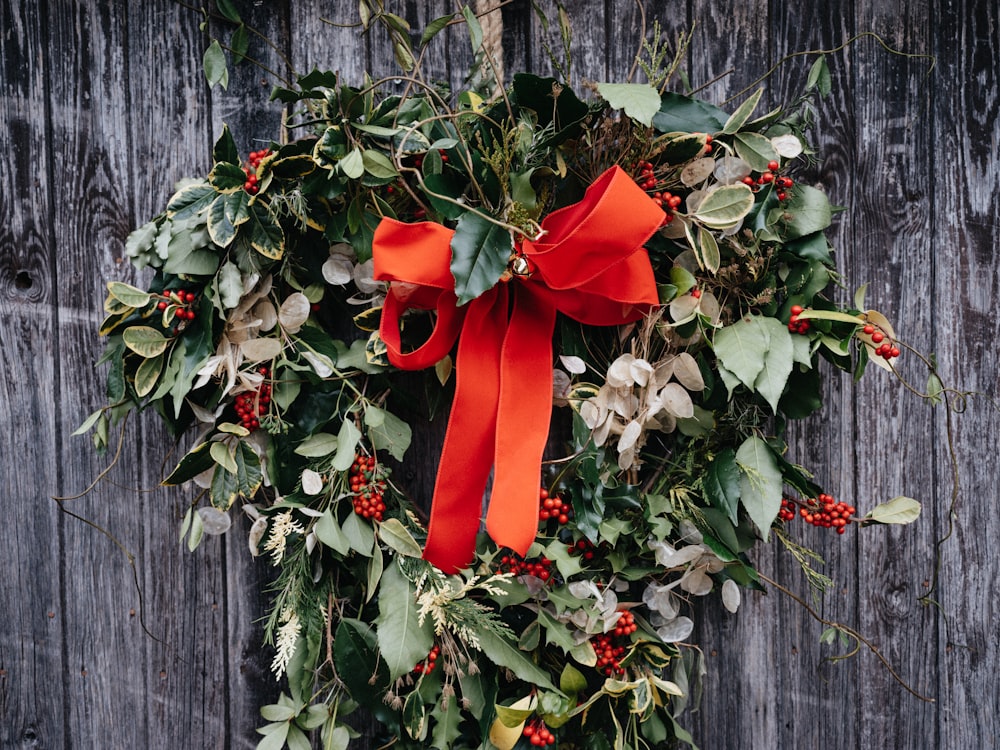 a wreath with a red bow hanging on a wooden fence