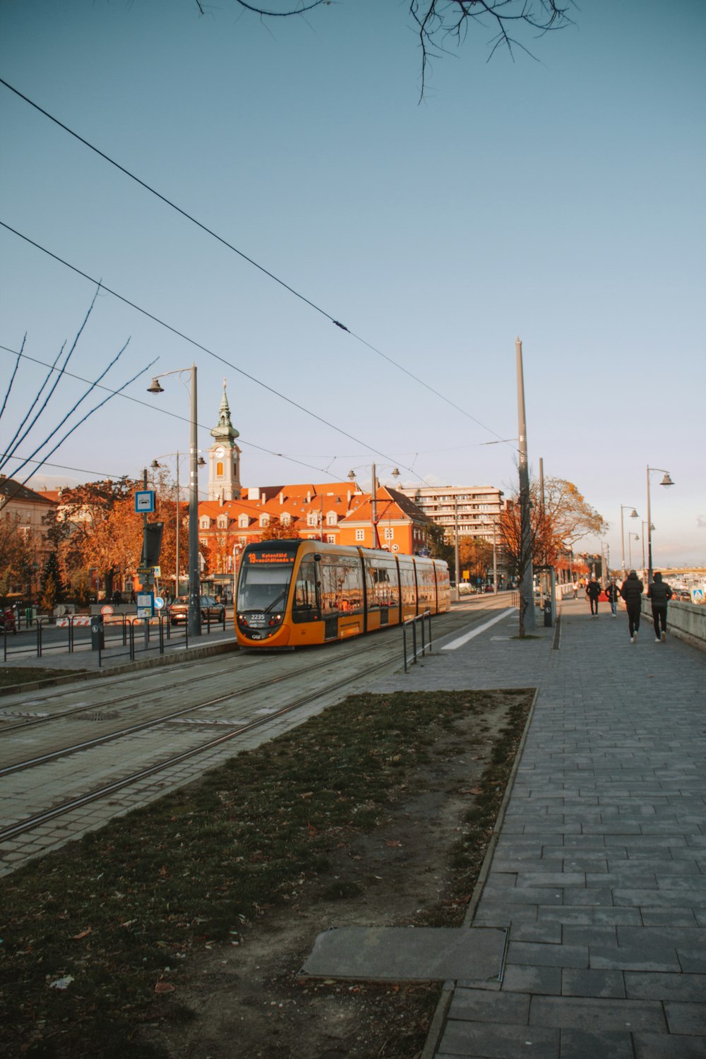 a yellow train traveling down train tracks next to a sidewalk