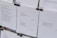 Several sheets of paper clipped together display various poems. The visible pieces contain poems discussing themes such as war, peace, and wishes for a better future. The text is printed in a clean, minimalistic font against a white background, with black clips at the top securing the sheets.