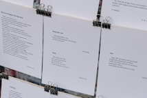Several sheets of paper clipped together display various poems. The visible pieces contain poems discussing themes such as war, peace, and wishes for a better future. The text is printed in a clean, minimalistic font against a white background, with black clips at the top securing the sheets.
