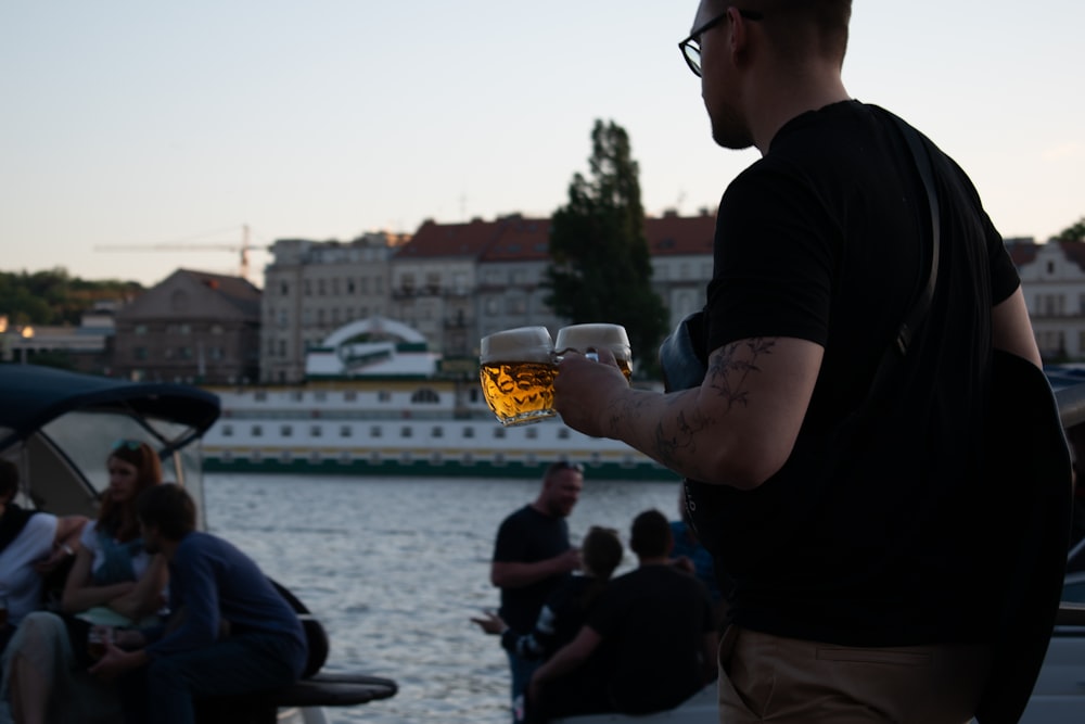 a man holding a glass of beer in front of a body of water