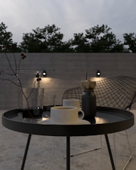 A classic outdoor side table made of weather-resistant metal, holding a lantern and a cup of coffee.
