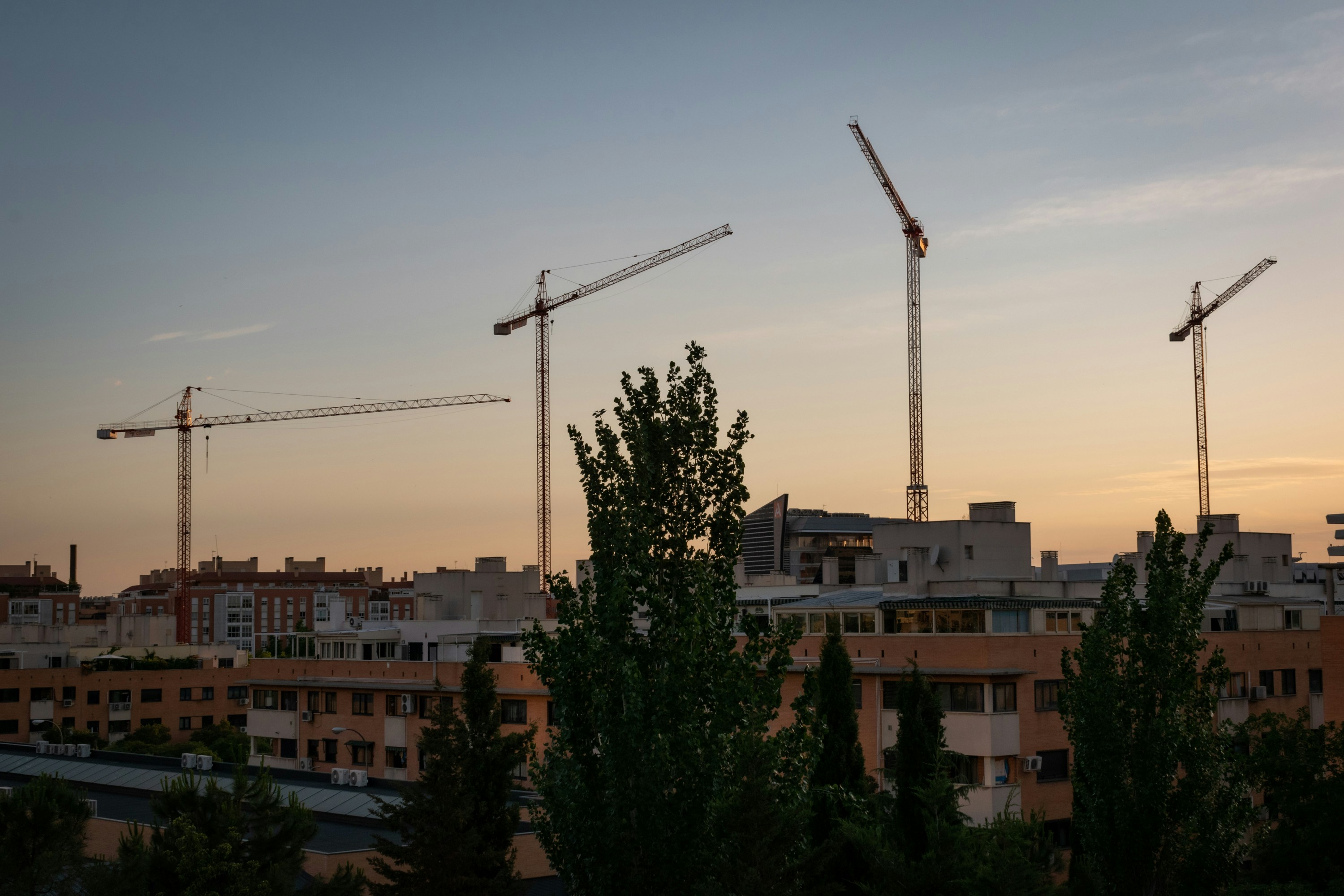 Construction site at sunset with cranes and steel structure against orange sky