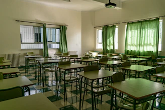 A professional cleaner in green uniform wiping a school desk with a forest green background.