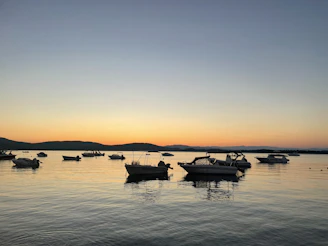 A serene boat gliding through the calm, deep blue waters of the Gulf of Poets at sunset, with the coastline of La Spezia softly illuminated in the background.