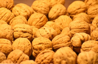 A collection of whole walnuts with their textured, brown shells piled together, creating a natural and organic appearance.