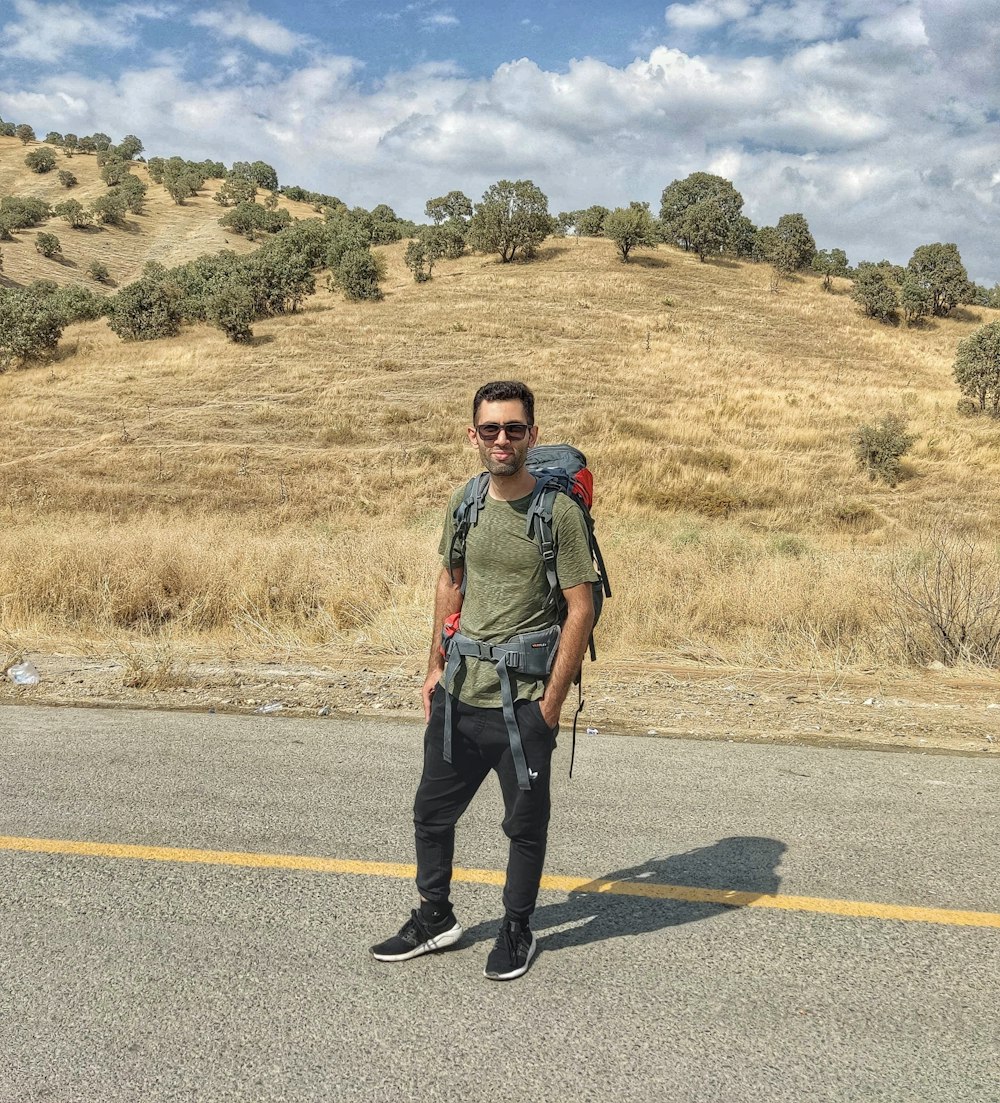 a man standing on the side of a road with a backpack on his back