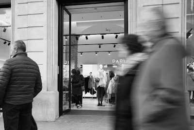 a black and white photo of people walking in front of a store