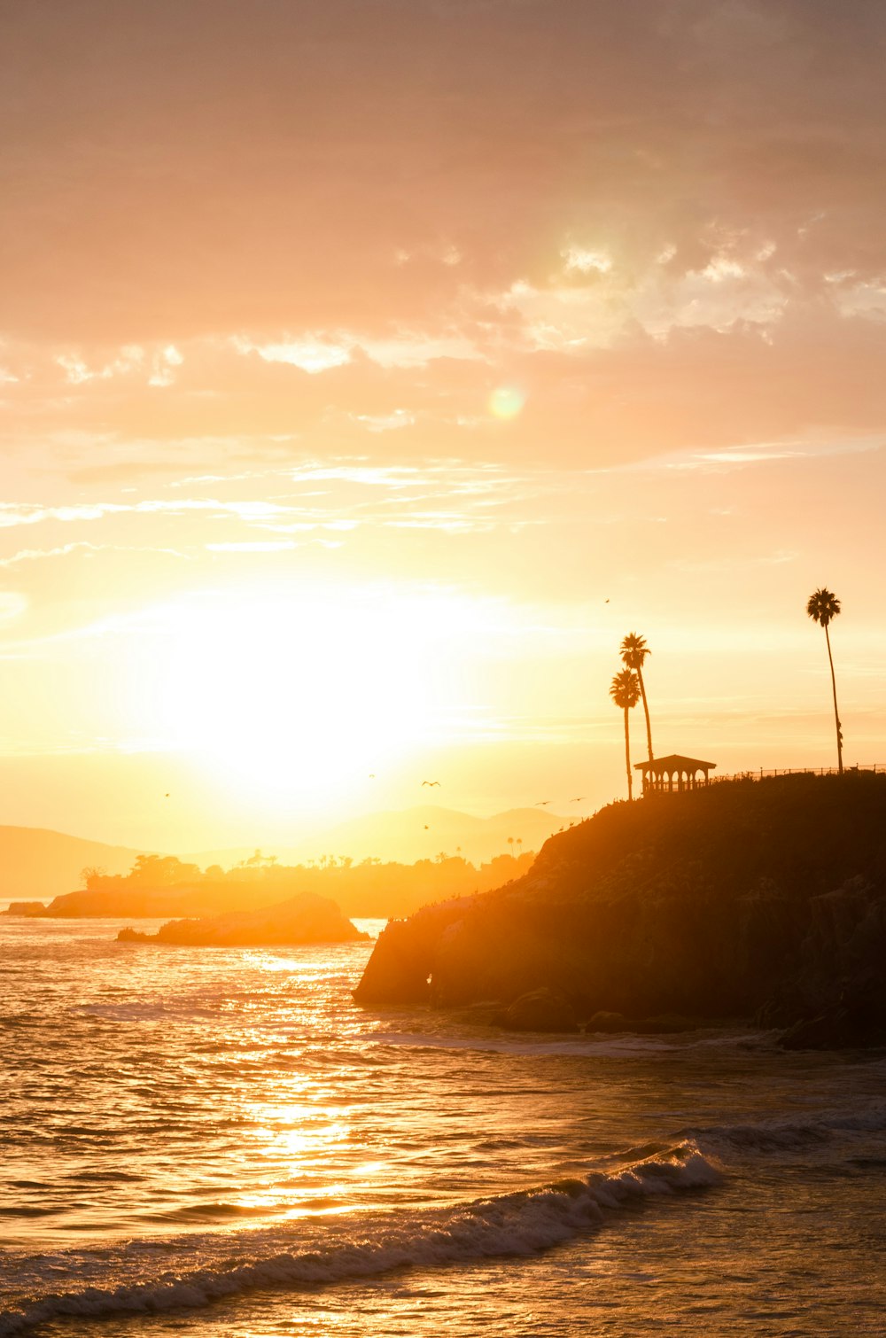 the sun is setting over the ocean with palm trees