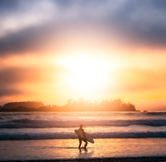a person walking on the beach with a surfboard in tofino