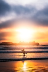 a person walking on the beach with a surfboard in tofino
