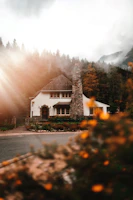 A cozy stone cottage nestled among vibrant autumn trees under a soft golden sunset.