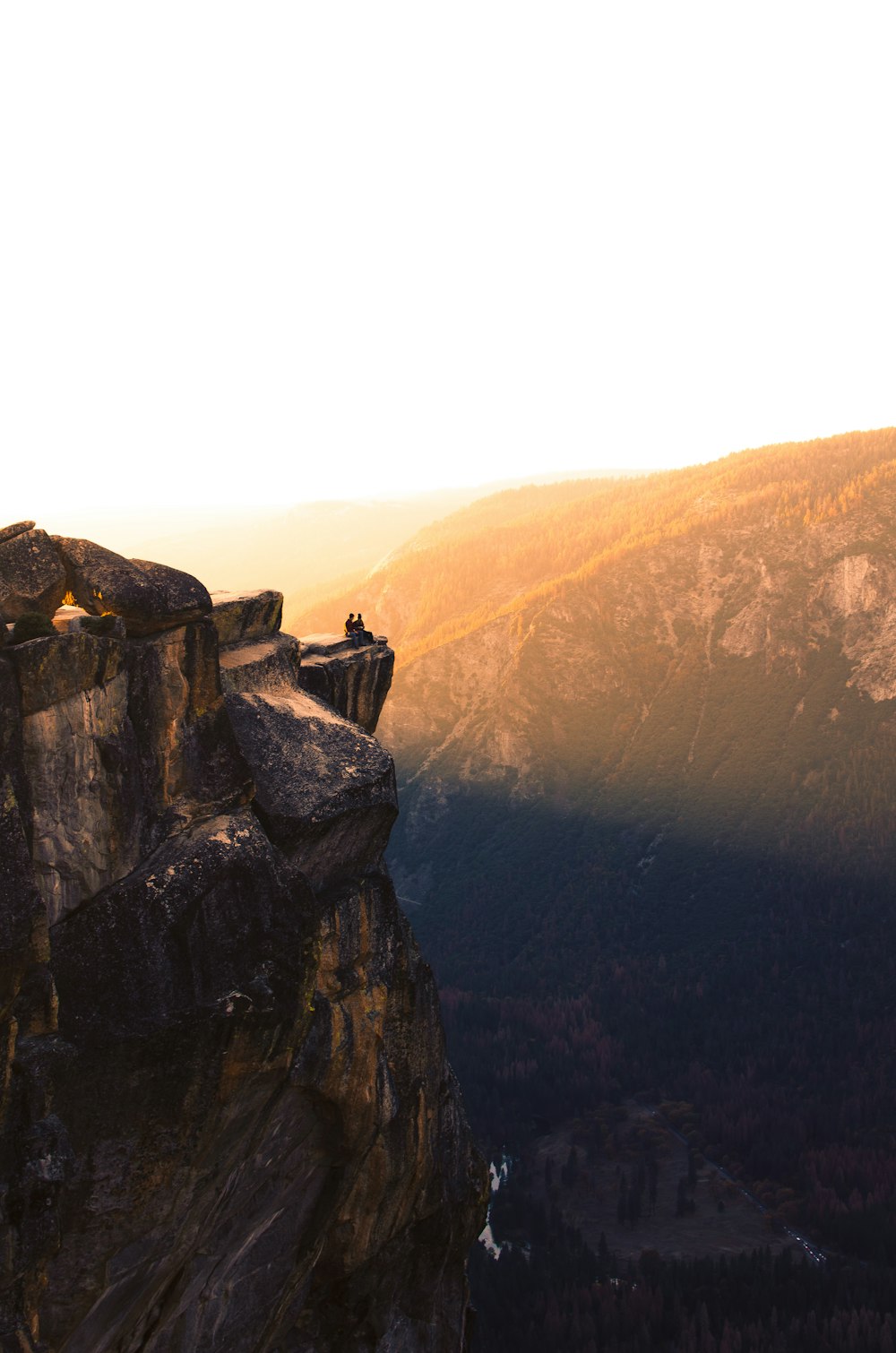 a man standing on top of a cliff next to a forest