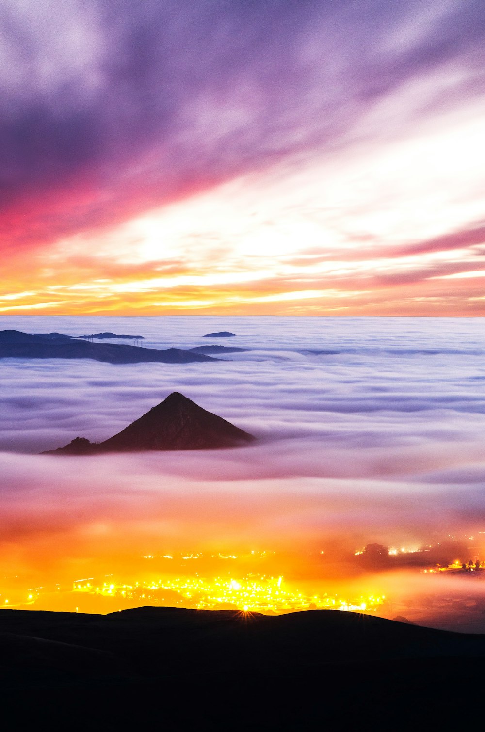 a view of a mountain in the clouds at sunset