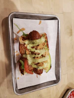 A loaded hot dog topped with crispy bacon, cheese, and smoky sauce on a warm bun.