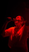 A candid shot of a female metal artist passionately singing into a vintage microphone under moody red lighting.