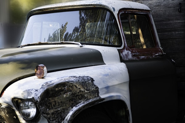 A weathered vintage truck parked beside a rustic wooden bookshelf filled with classic novels.